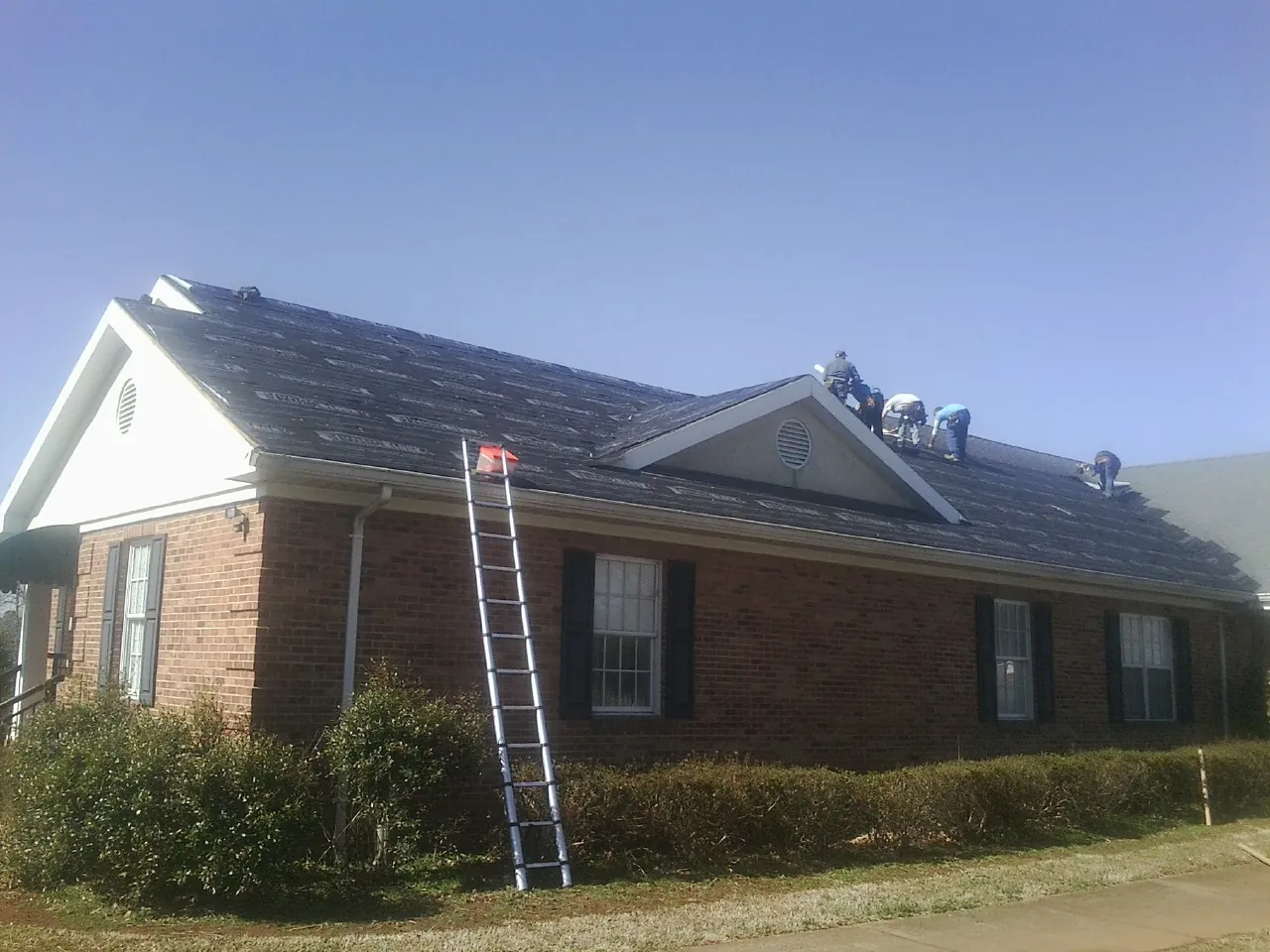 Crew tearing shingles off a brick ranch roof with a ladder set — Metal Roof Repair work by our crew in Broad Brook