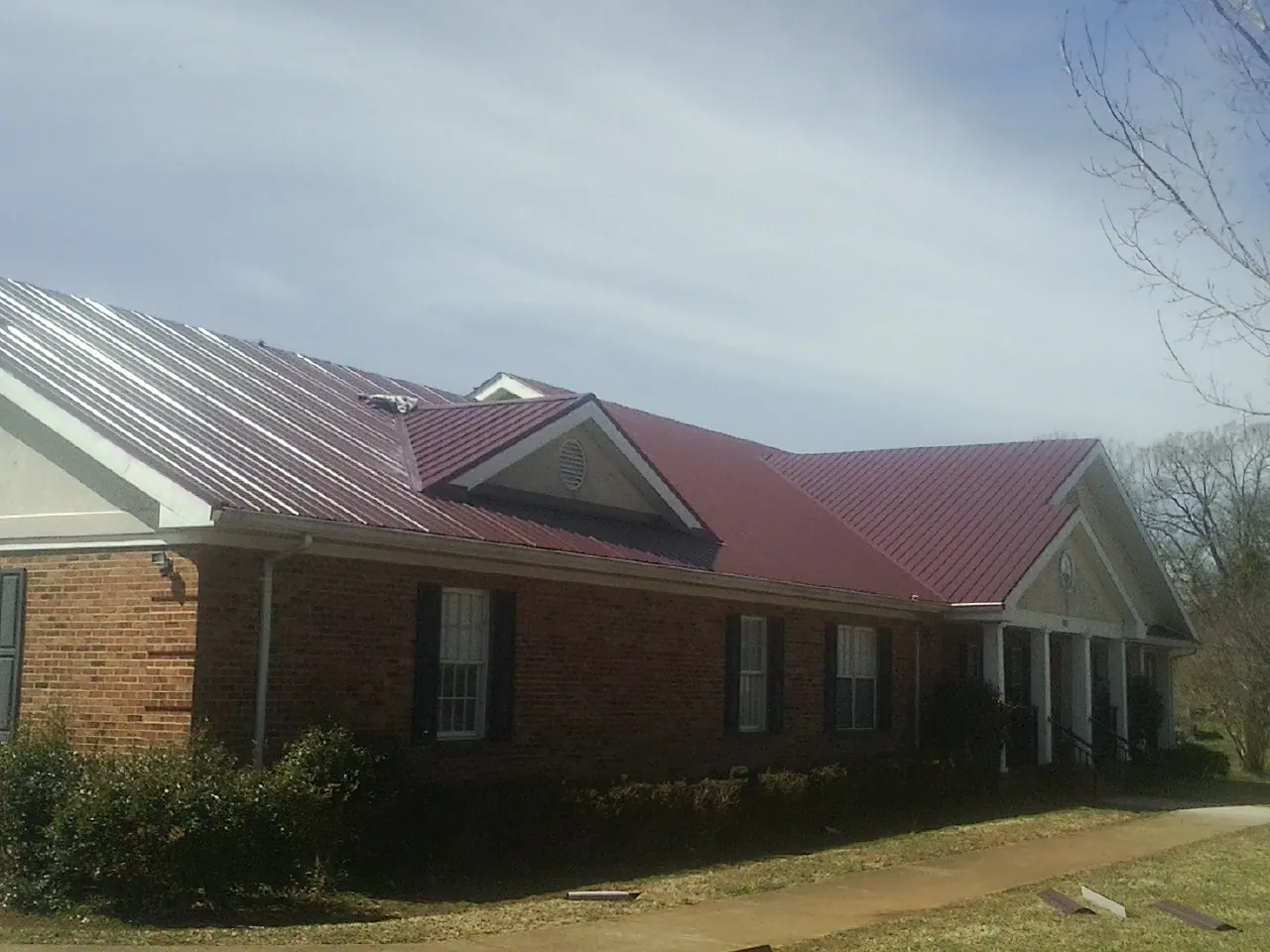 Red metal roof with gabled entries on a long brick building, from a Hail Damage Roof Repair job in Broad Brook
