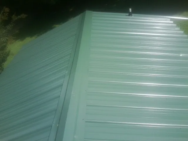 New green metal panels meeting at the ridge of a roof — Flat Roof Repair work by our crew in Broad Brook