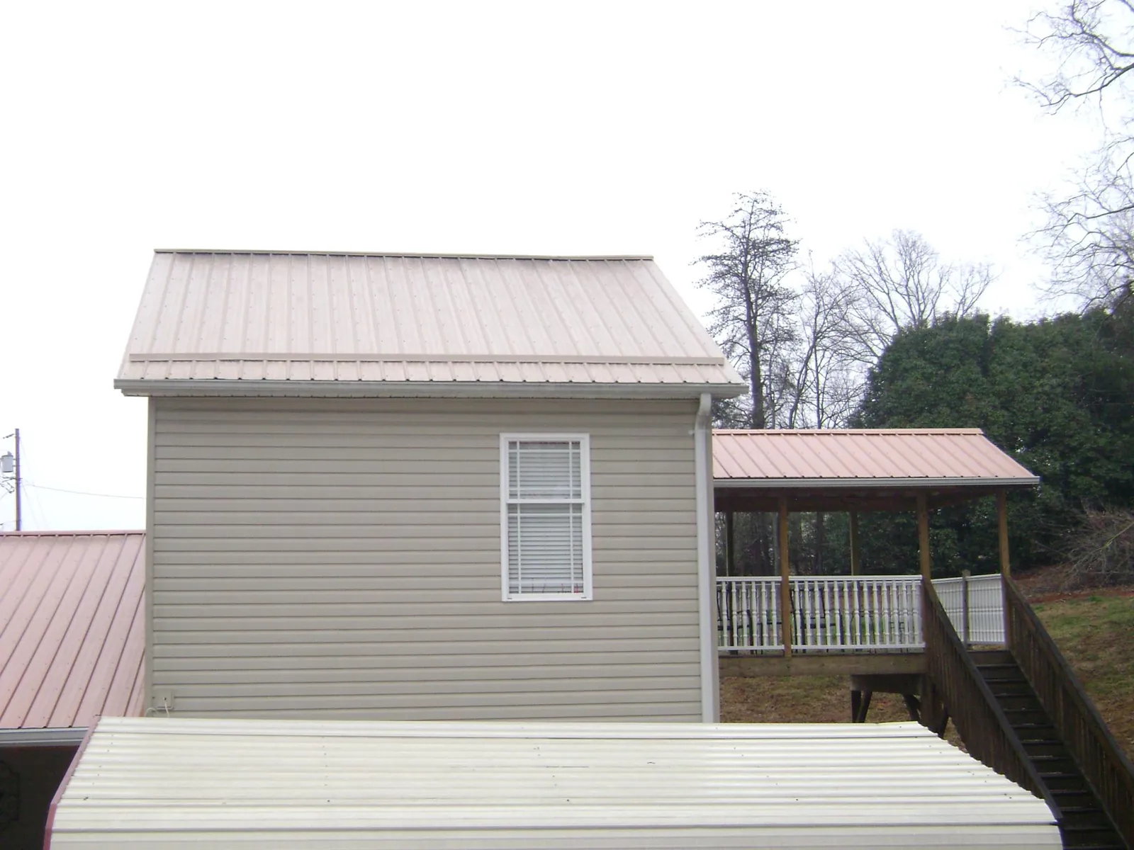 Tan metal roofs on a two story addition and attached porch, from a Roof Replacement job in Broad Brook