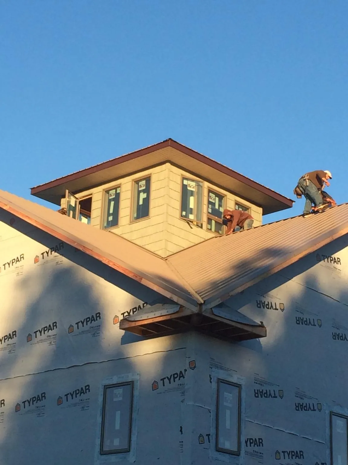 Roofers working around a rooftop cupola on a new metal roof at sunset — Roof Waterproofing in Broad Brook by Roofing Brothers